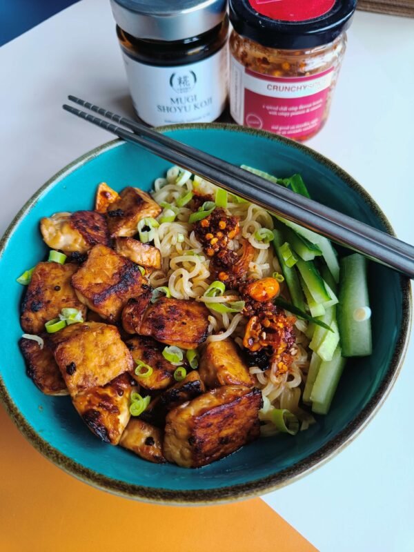 A bowl of noodles with grilled tempeh, crunchy spice crispy chili oil, cucumber, chili crisp, chopsticks